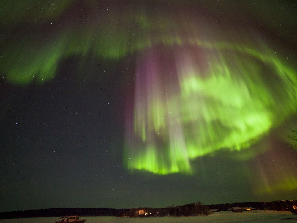 An image of the northern lights over Lake Inari in Finland. The lights are a glowing green and purple.