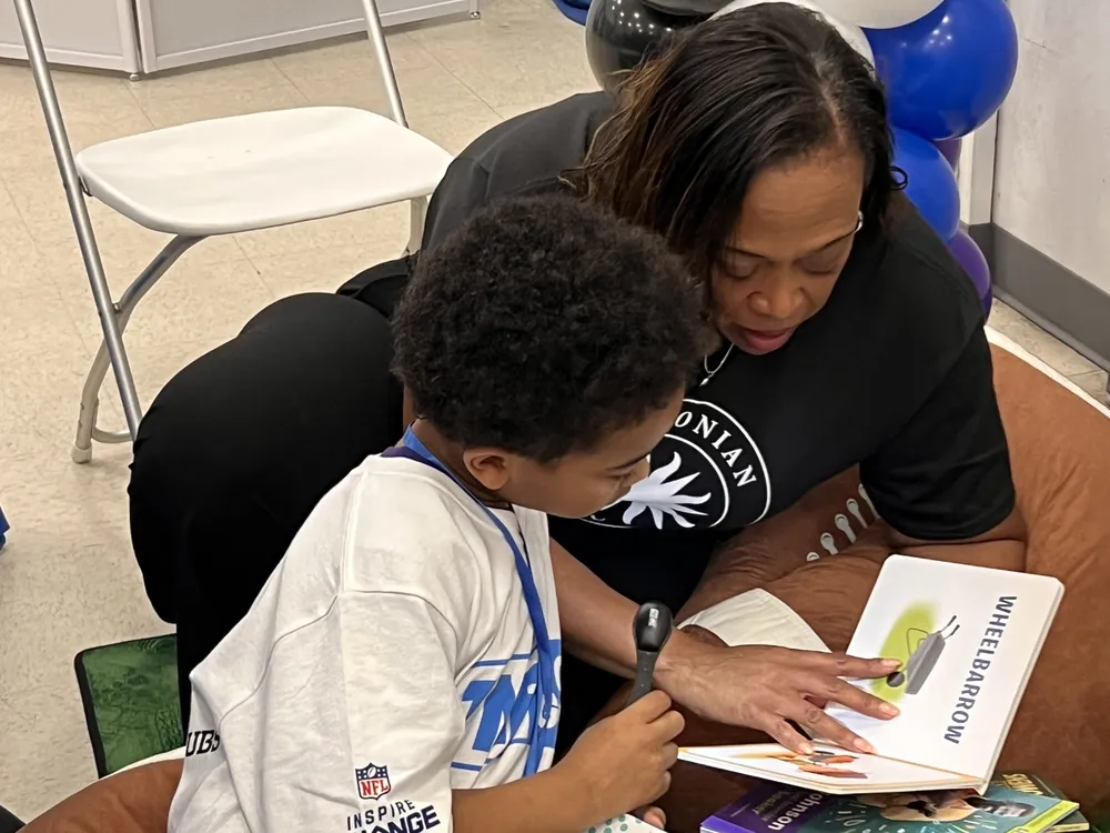 A woman reads with a young boy, the book says "wheelbarrow" in big letters