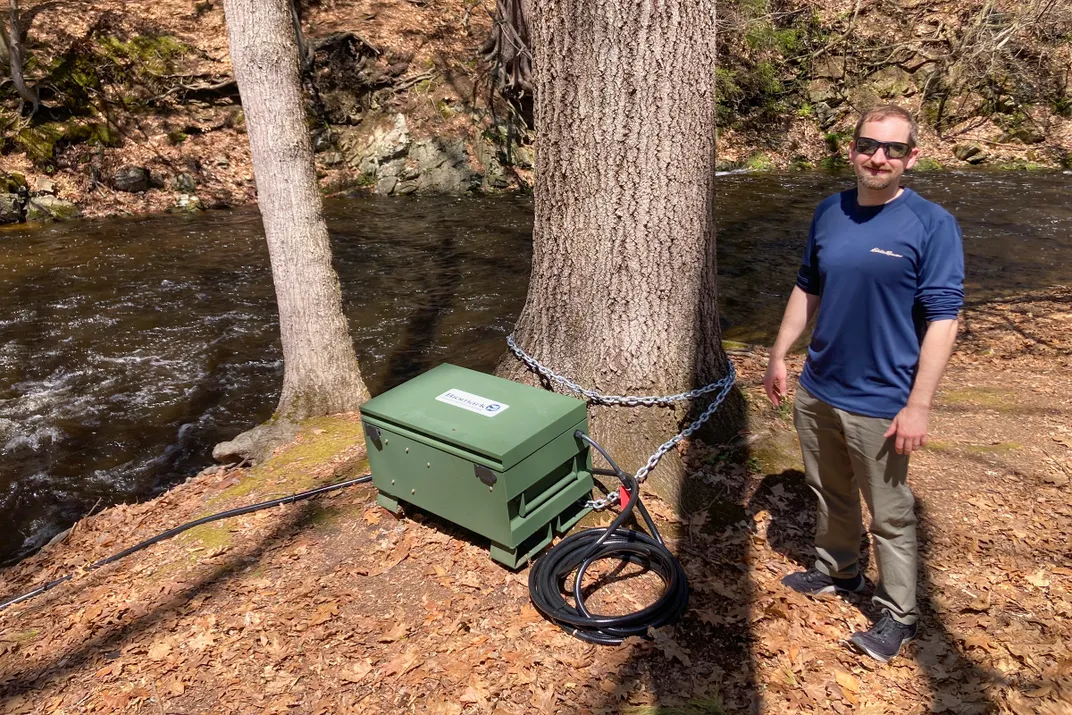 a man stands next to a tree with a green box attached to it