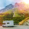 Sun shines brightly on a mountain landscape scene depicting a road with an RV