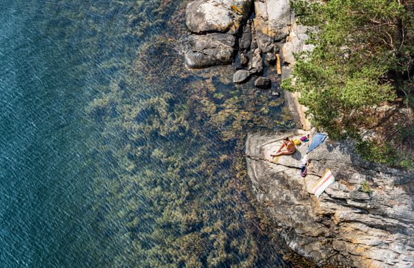 A woman enjoys a sunny day all alone on a rocky shore by a crystal clear water thumbnail