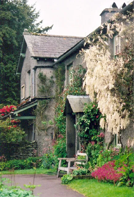 A view of the front door of a cottage covered in crawling vines and pink flowers