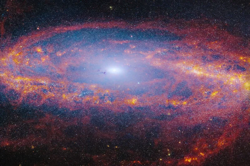 A spiral galaxy with a blue-white, glowing core seen at an angle, from above. The disc is filled with waves and strands of bright red, orange, and yellow