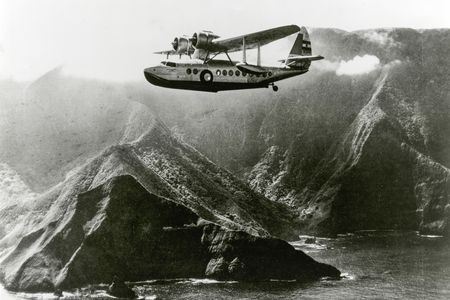 An Inter-Island Airways Sikorsky S-43 flies past Molokai mountains and lagoon.
