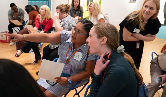 Two teachers sit side by side pointing out details in a museum gallery