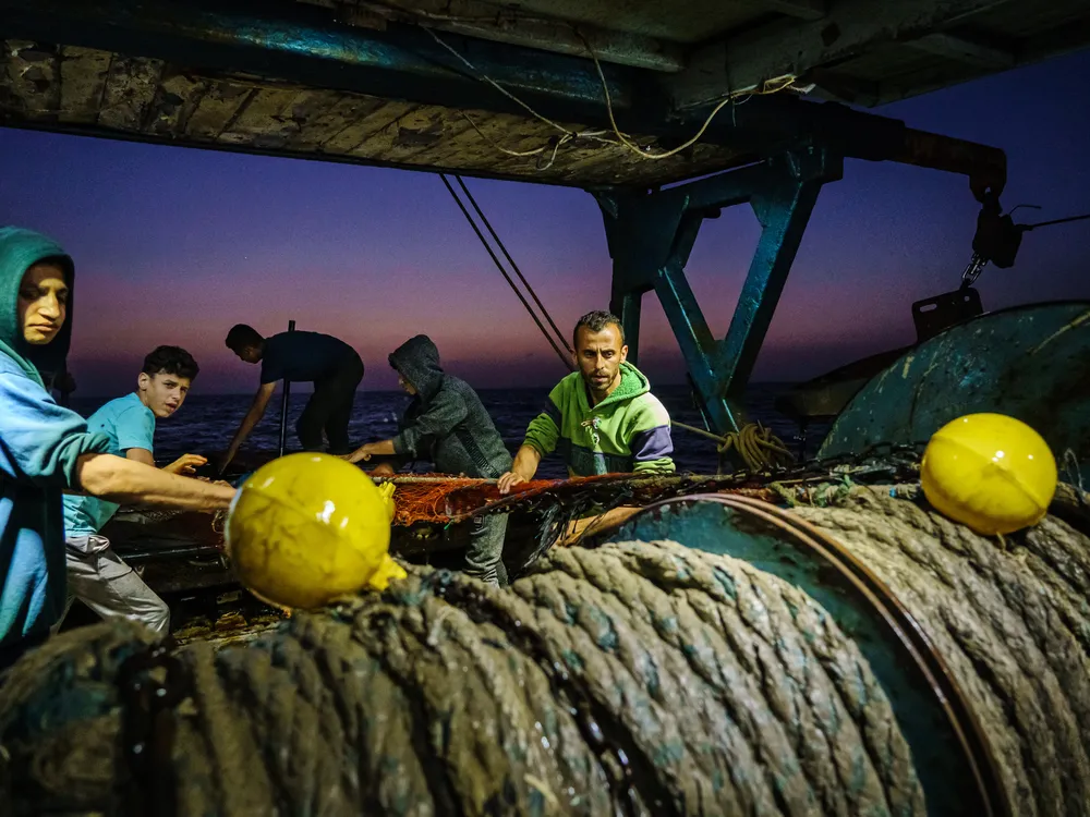 Fishers pull rope by hand at dusk on a fishing vessel in Gaza