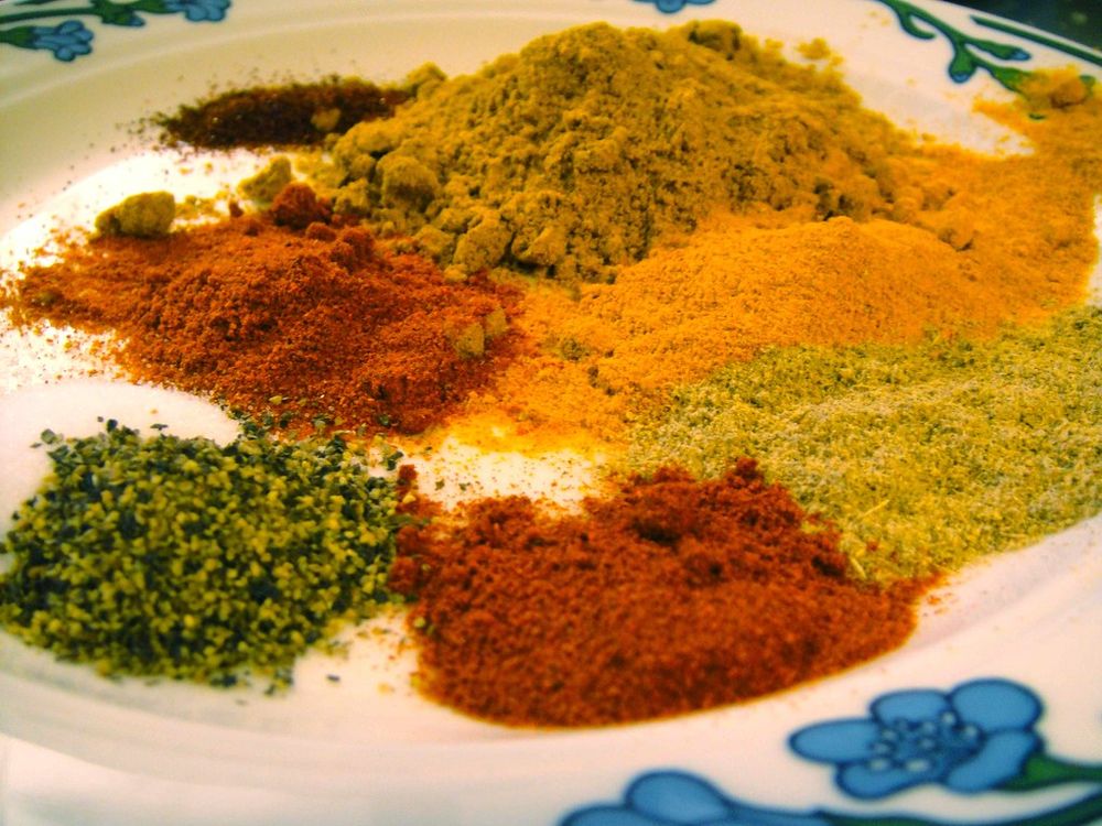 piles of red, brown, orange and yellow spices on a white plate with blue flowers around the rim