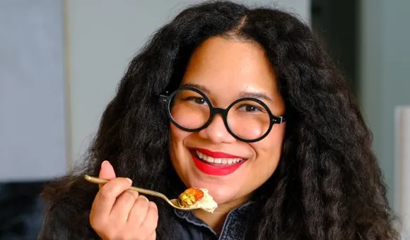 Image shows a smiling woman eating a bowl of fruit.