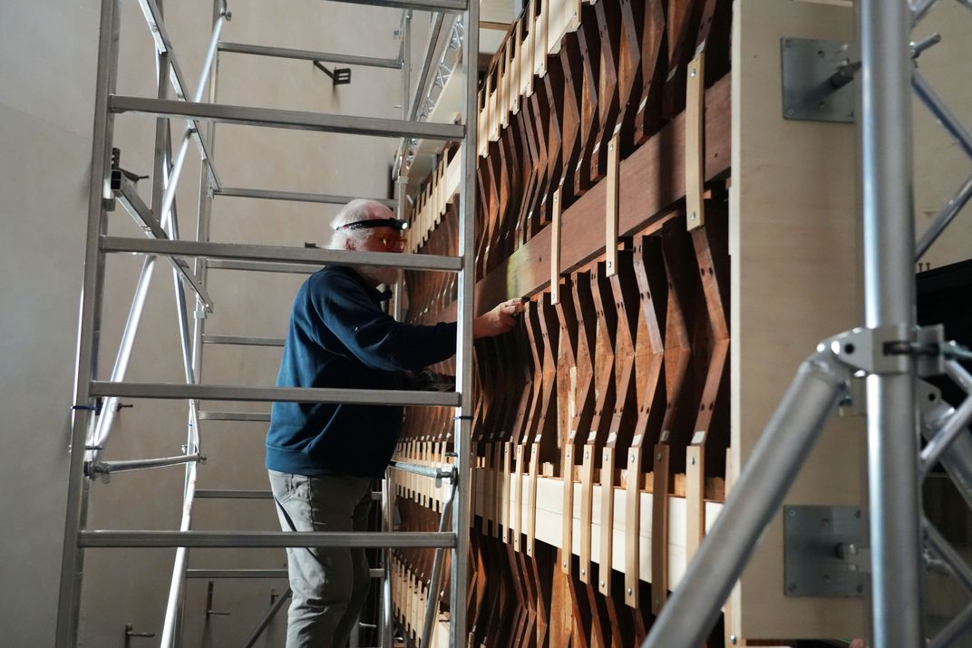 Man working on scaffolding on the back of wooden paneling