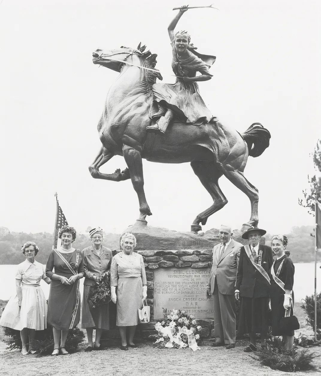 a group of people stand in a portrait in front of a statue of Sybil Ludington