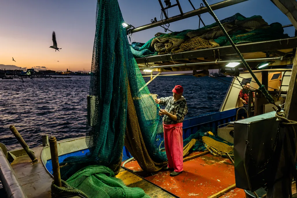 Fisherman fixing a net on a boat at dusk