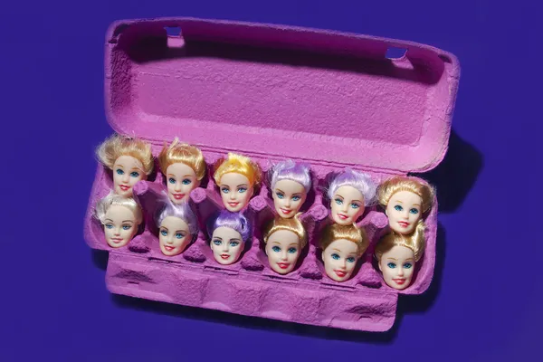 A Dozen Doll Heads Displayed in a Bright Pink Egg Carton thumbnail