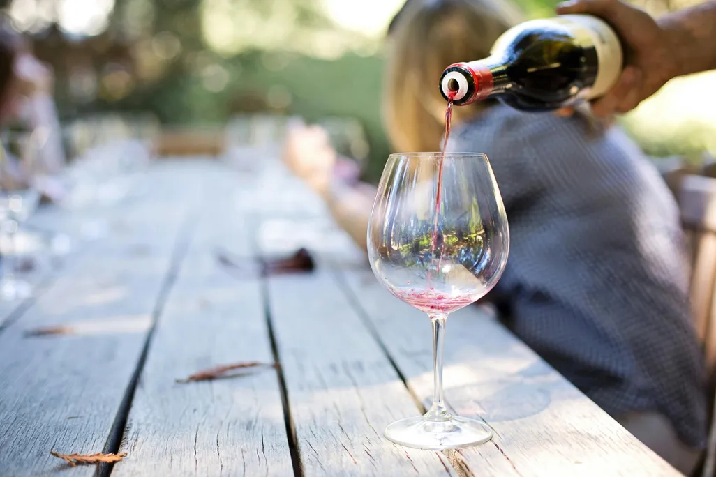 Hand pouring a glass of wine from a bottle on a wooden table
