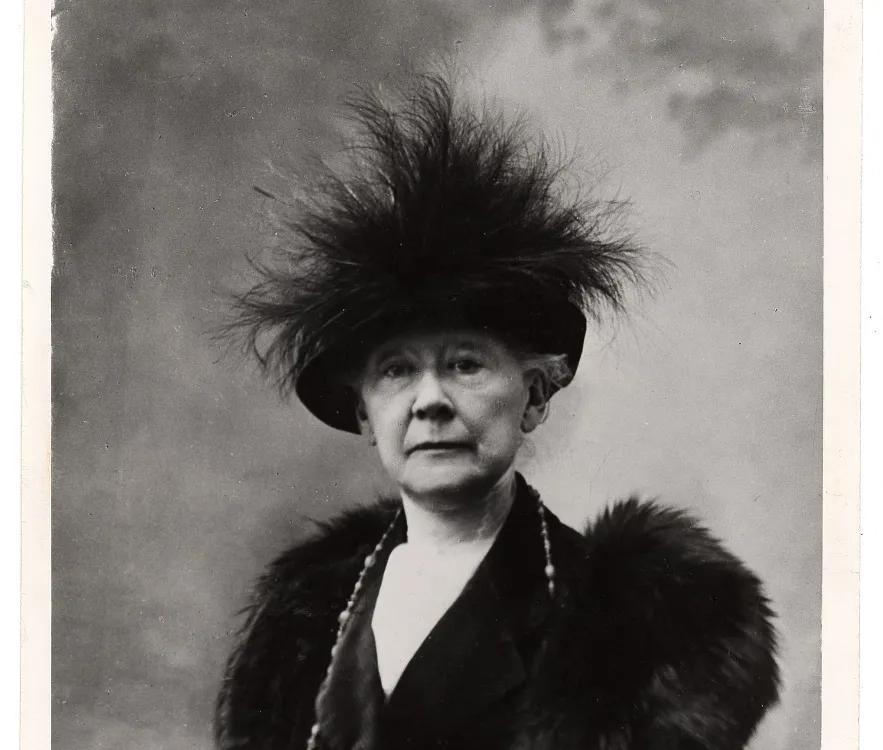 Black and white portrait of Mary Cassatt sitting in a chair wearing fur and a feathered hat.
