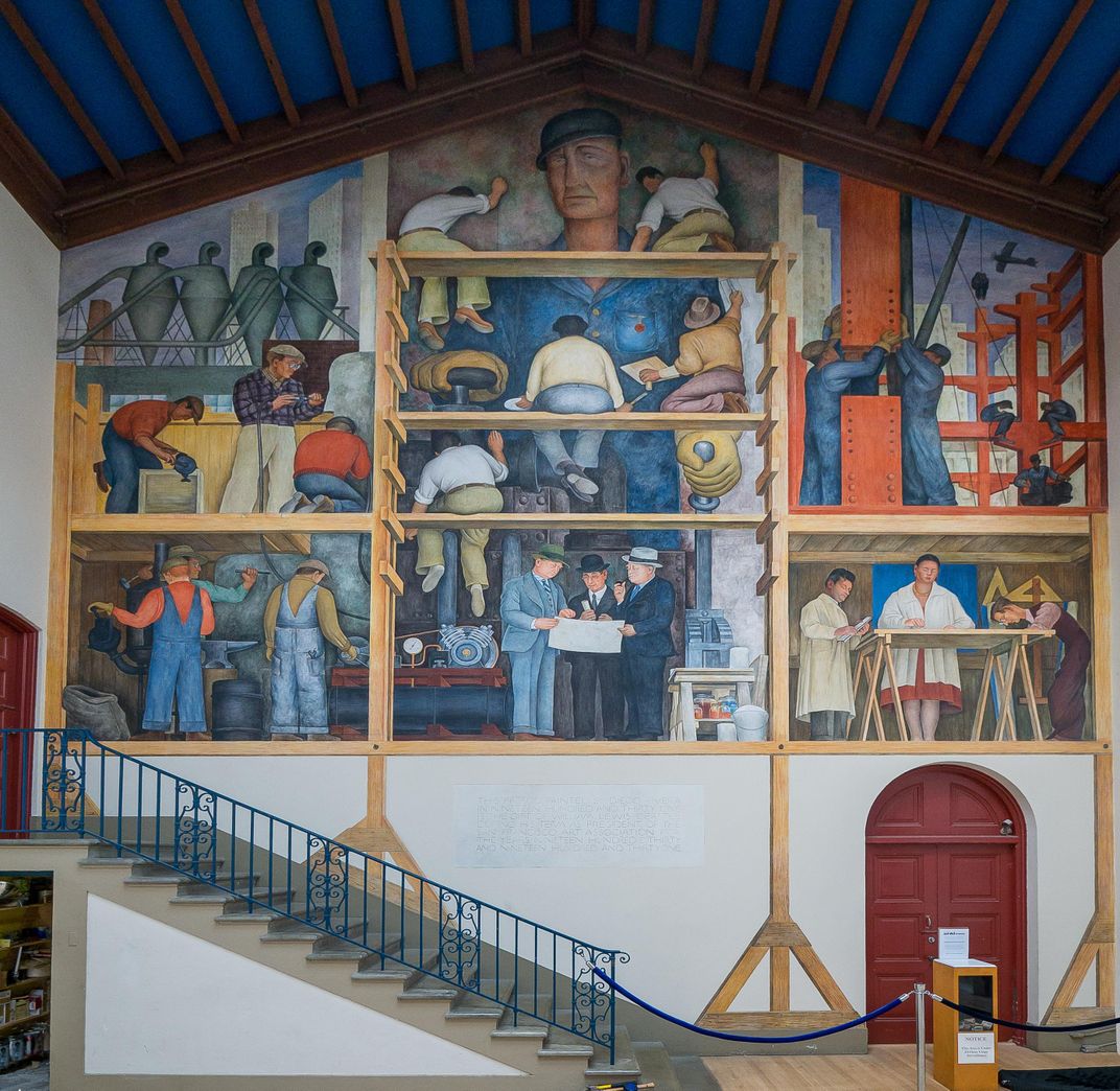 A wider shot of the room, with a curved red door visible beneath the mural and a staircase to give a sense of scale. The mural is very big and reaches up to the top of the peaked ceiling