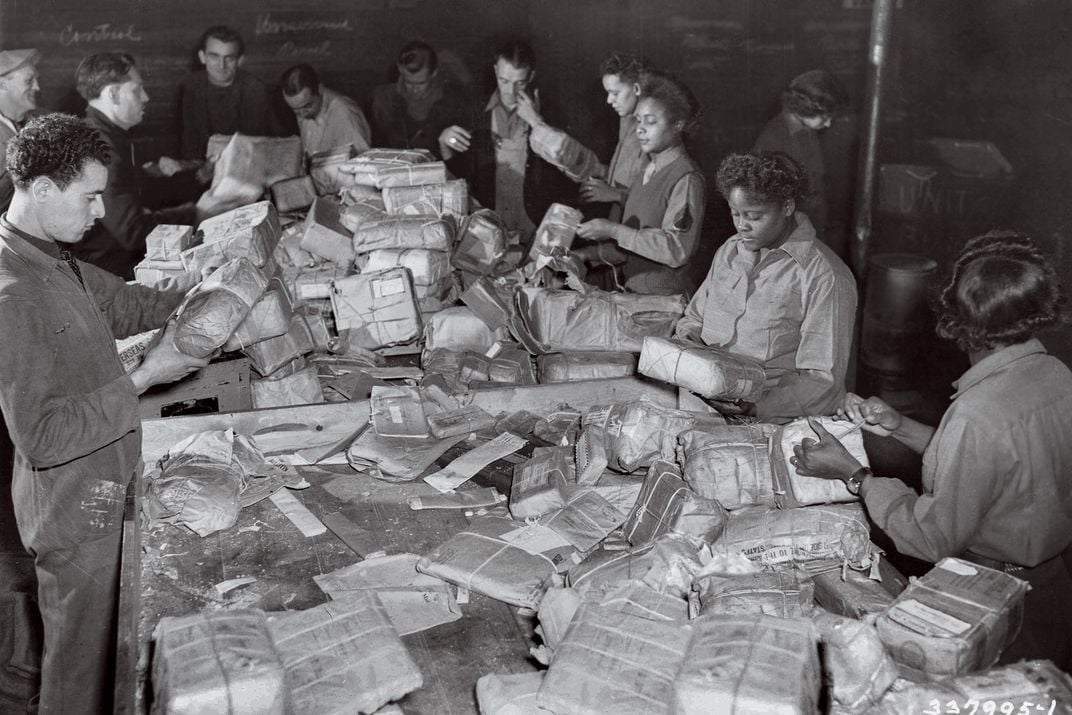 a black and white photograph of men and an all Black woman military unit sorting mail during world war two