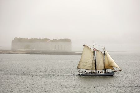 Flying Maine&rsquo;s original state flag, from 1901, the schooner Timberwind sails out of the fog, past Fort Gorges in Casco Bay.