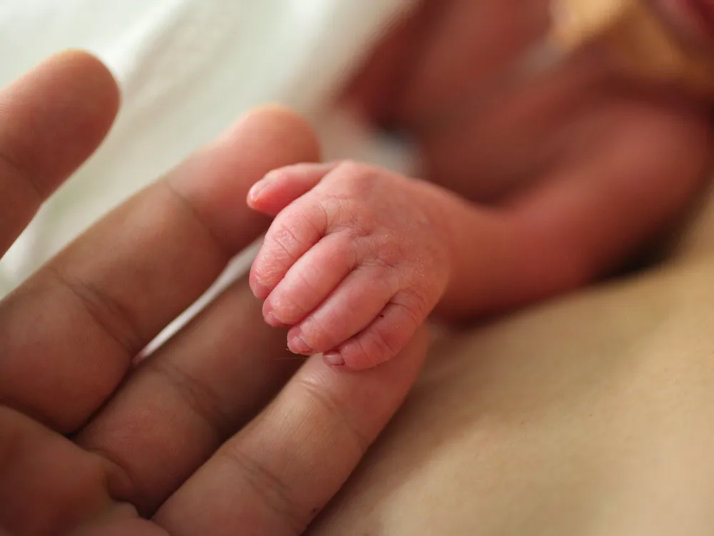 A hand of a prematurely born baby rests on the fingers of an adult
