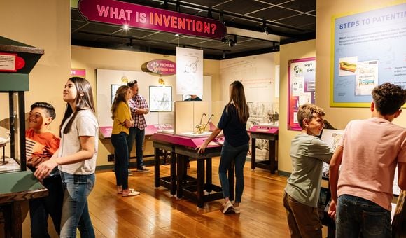 Seven people- adults and children- interact with the Nation of Inventors exhibition gallery