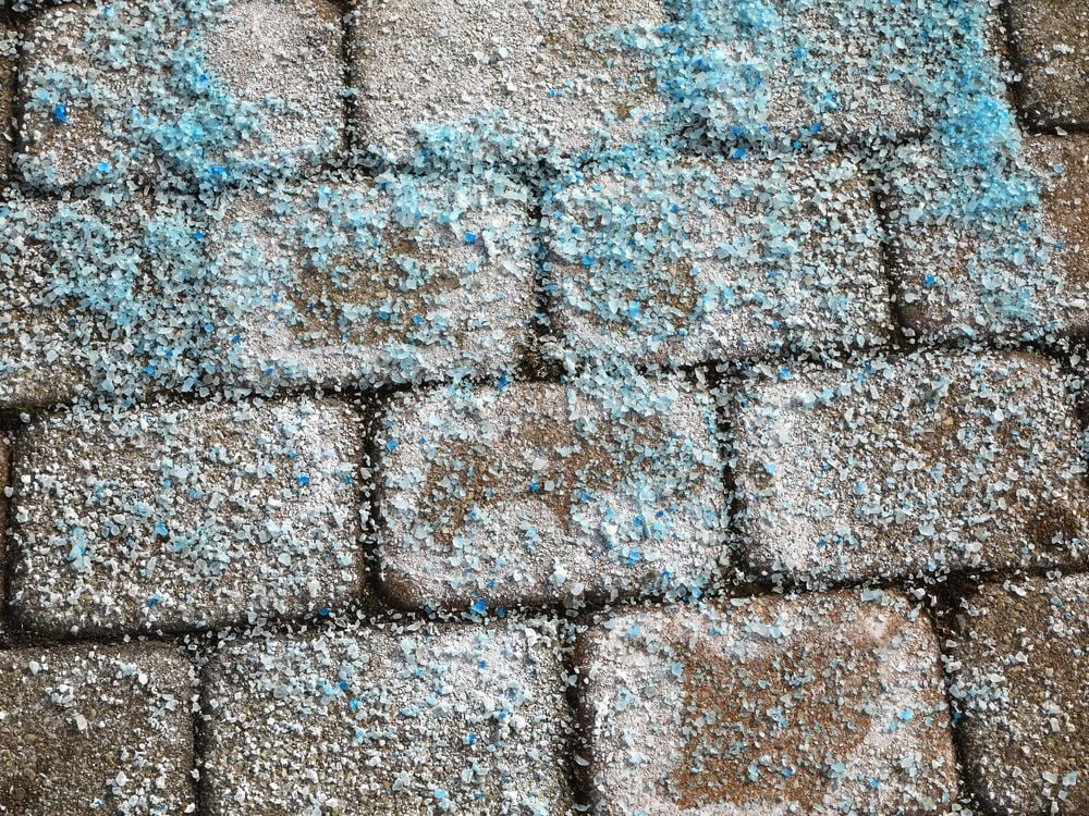 An image of blue road salt covering an icy brick road.