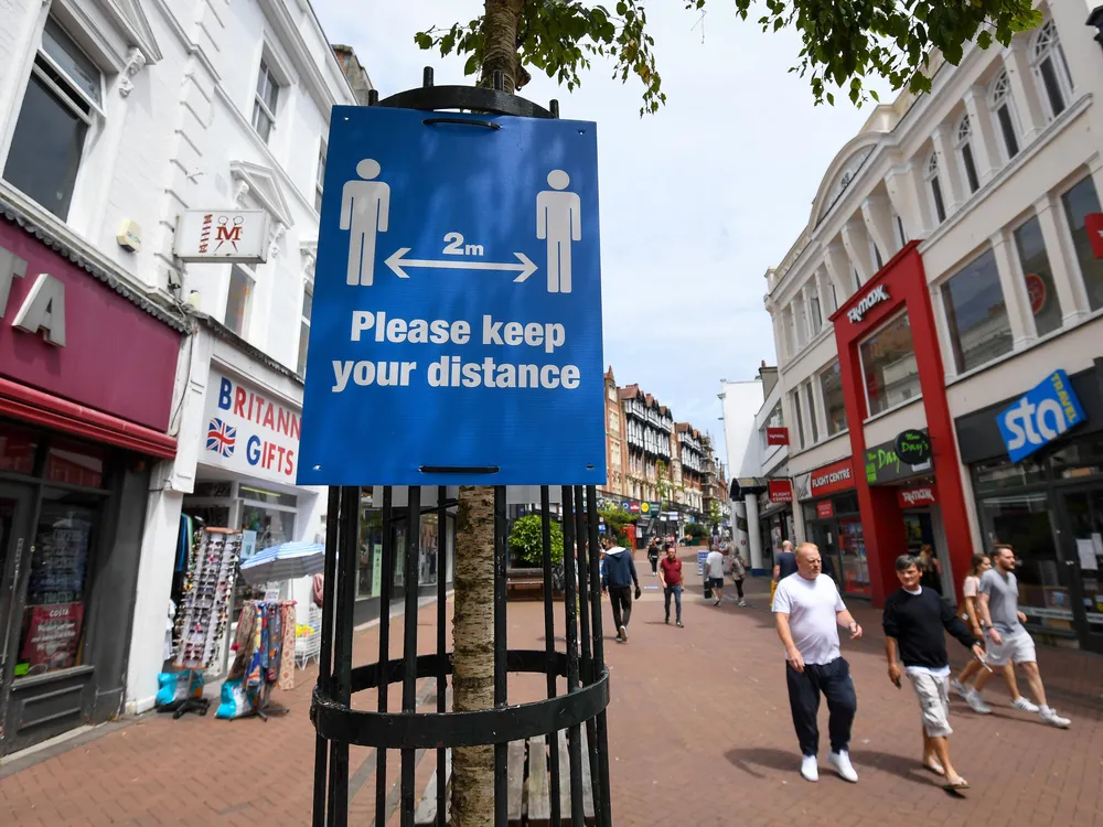 A sign reads "Please keep your distance" on a street with small shops in Bournemouth, U.K.