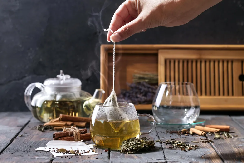 Hand holding tea bag by string over hot cup of tea