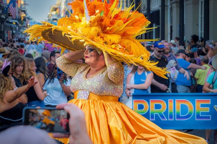 a person wearing giant yellow hat in a yellow dress during a Pride parade