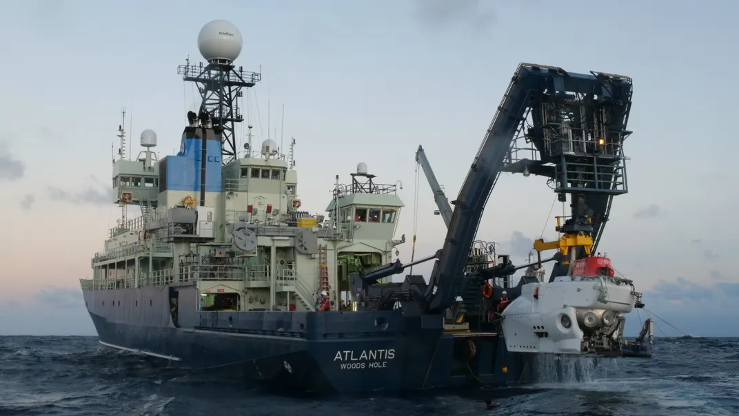 ship with an arm lifting a white submersible vehicle