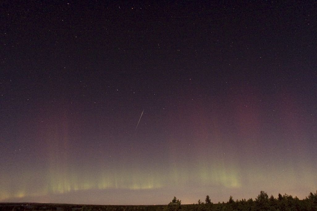 a draconid meteor streaks across the sky with the northern lights visible