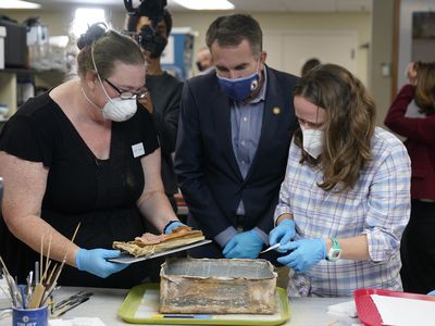 Virignia Governor Ralph Northam (center) looks on as conservators Kate Ridgway (left) and Sue Donovon (right) remove the time capsule&#39;s contents.