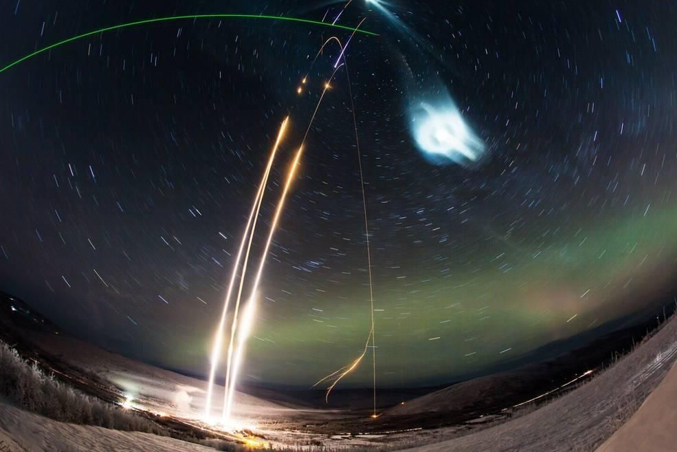 A photo of a NASA's Super Soaker Rocket creating a glowing noctilucent cloud. The photo shows a shining blue orb. 