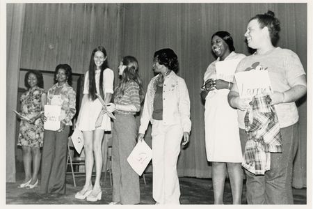 Candid photo of seven women holding papers standing in a line on stage.