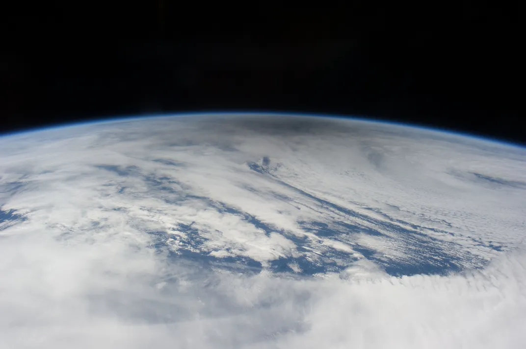 a shadow over cloud-covered ocean on earth seen from above, with dark space in the background