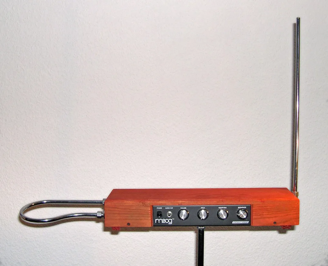 An orange box with buttons that resembles a radio, with a loop of metal jutting out its side (our left) and a long metal pole sticking up at a right angle on the other side, like a radio antenna (our right)