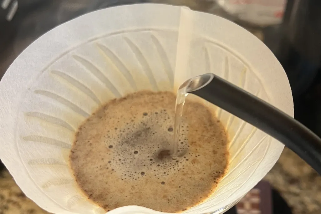 coffee grounds and water in a coffee filter as a goose-neck kettle pours a flow of water in