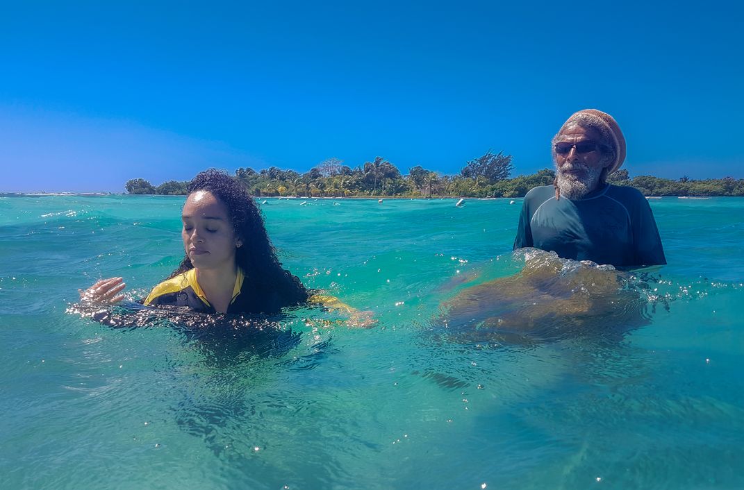 Two people swim in bright blue-green Belizean water.