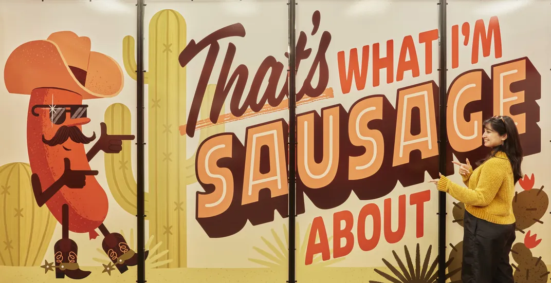 Large mural that says That's What I'm Sausage About with a woman in front of it