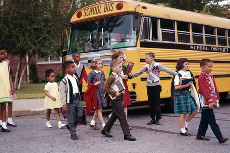 Children cross the street in front of a yellow school bus in 1965.