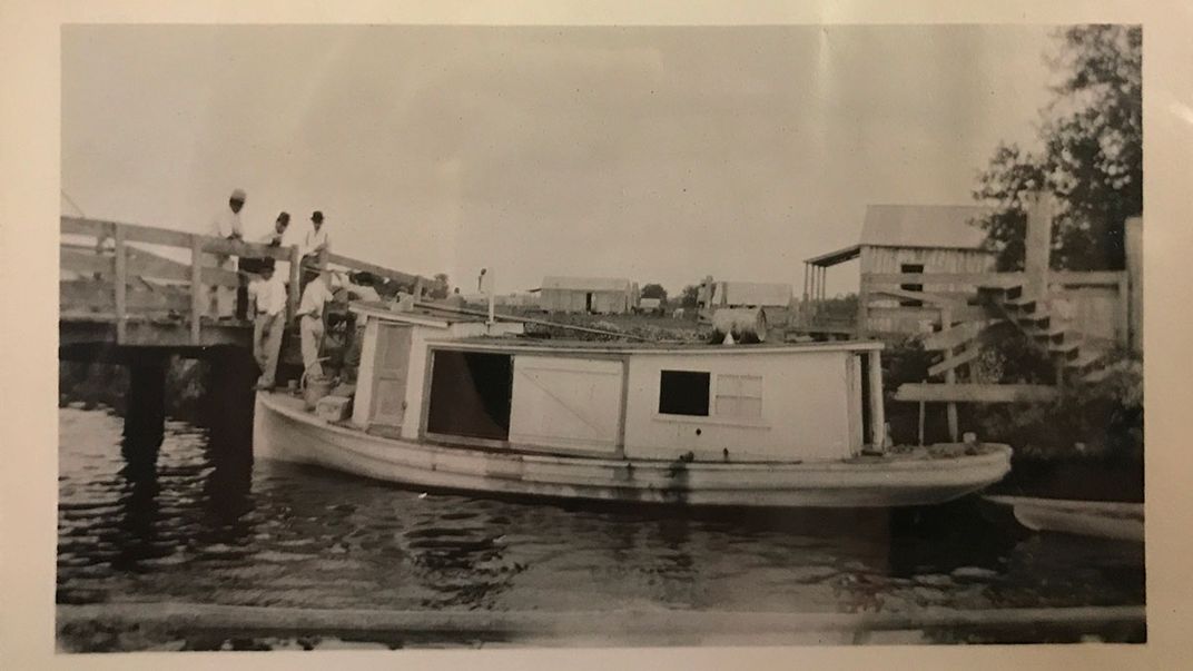 A boat docked on a river. Black-and-white photo with one corner ripped off.