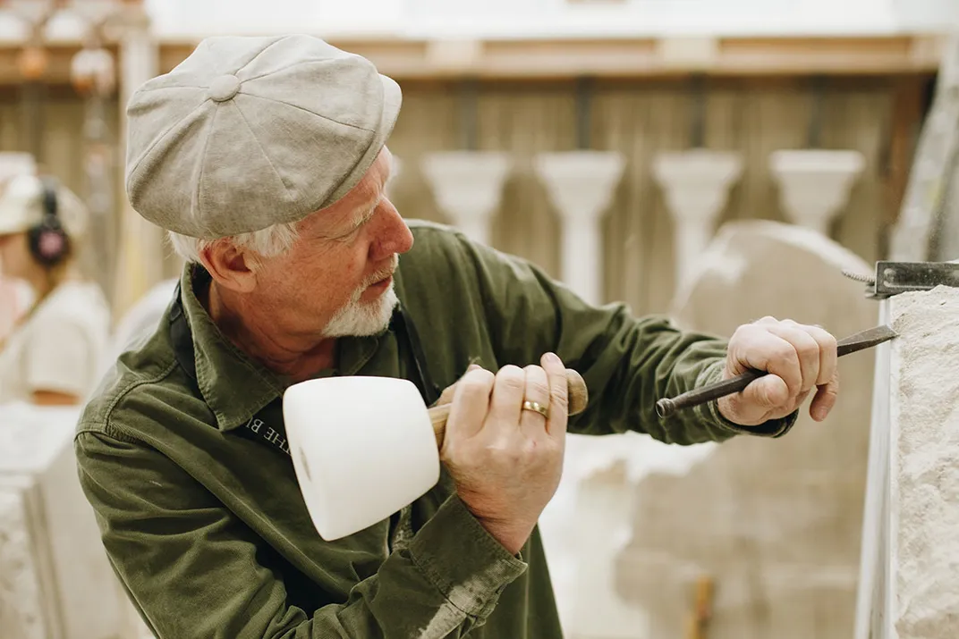 A man uses a mallet and a chisel to carve a large block of white stone.