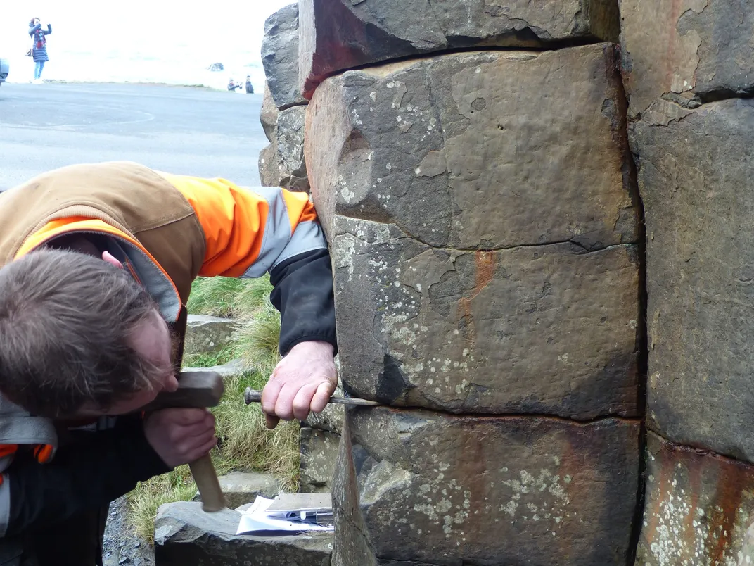 Person bending over and removing coin from between rocks