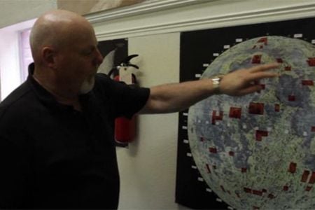 Dennis Hope stands next to a map of the Moon, showing (in red) all the plots of land he’s sold.