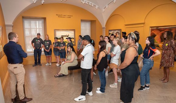 A man in a navy blue shirt and khakis leads a large group of students through an art gallery