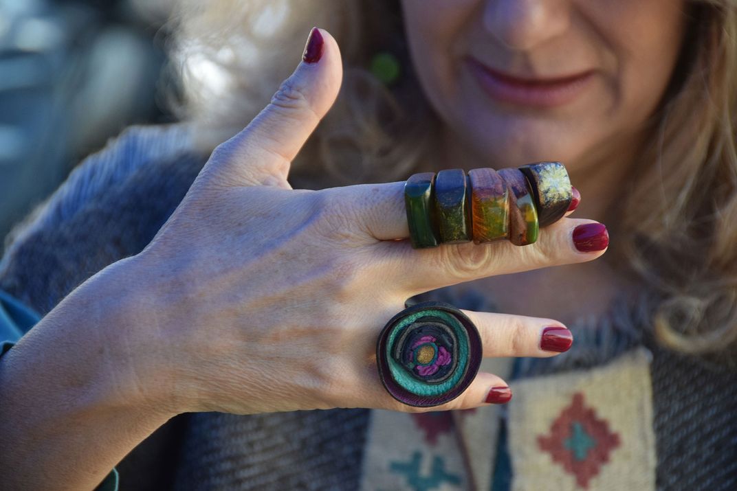 A woman holds her hand in front of her face. On her fingers are several brightly colored, glass rings.