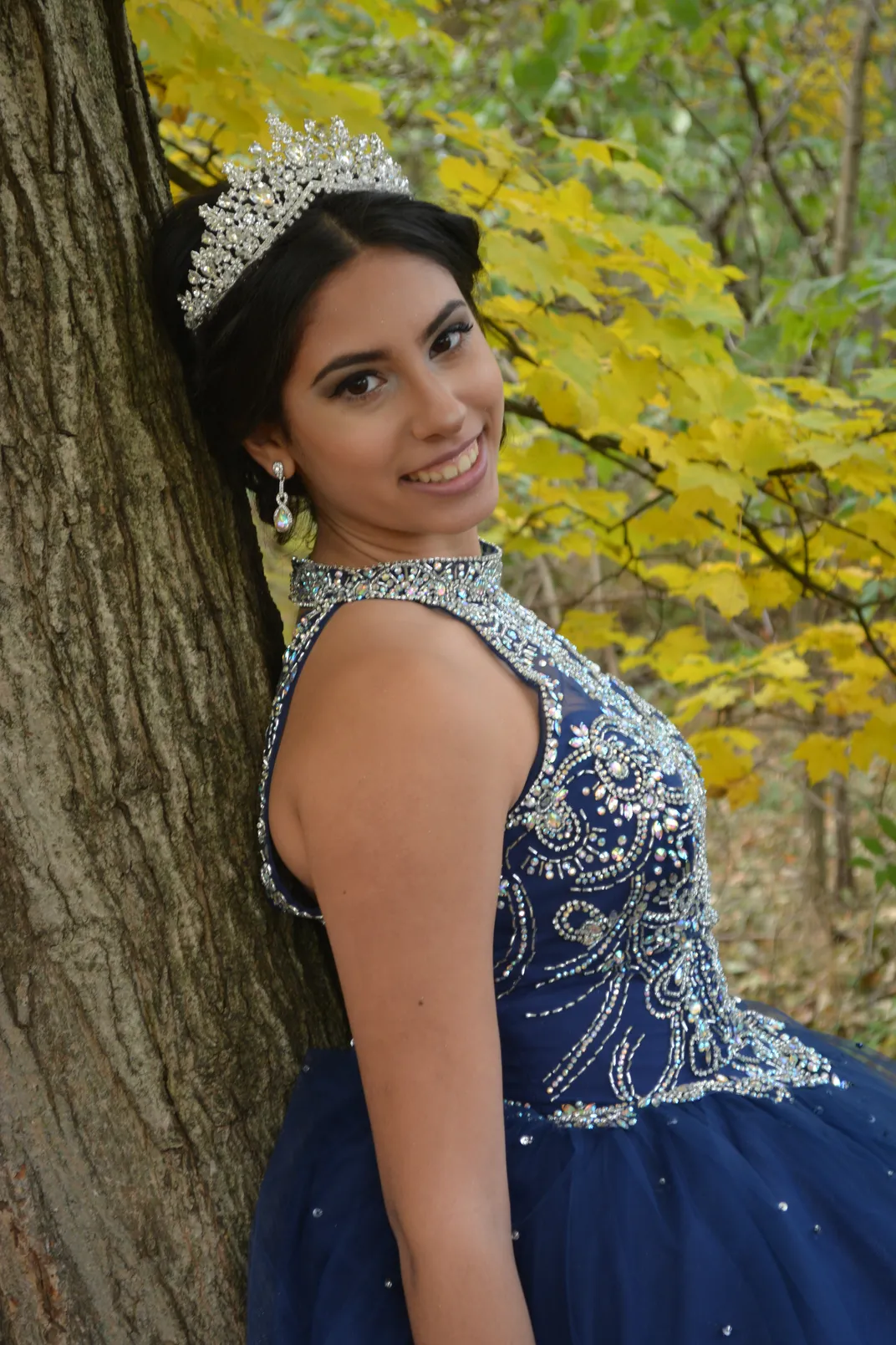 a woman in formal dress and crown leans on a tree