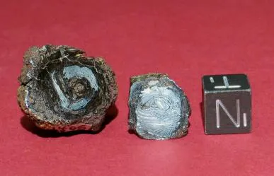 Photograph of two Havana meteoritic metal beads with a 1 cm cube for scale. The bead on the left (7.8 g mass) is cut perpendicular to the central hole, illustrating the extensive alteration of the bead and infilling of the central hole. The bead on the right (4.6 g mass) is cut parallel to the central hole and exhibits a concentrically deformed structure.