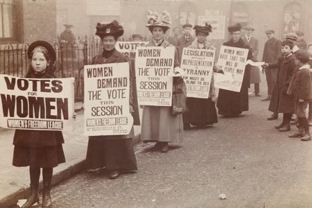 Women stand in gutter for a poster parade organized by the Women's Freedom League to promote the suffrage message.