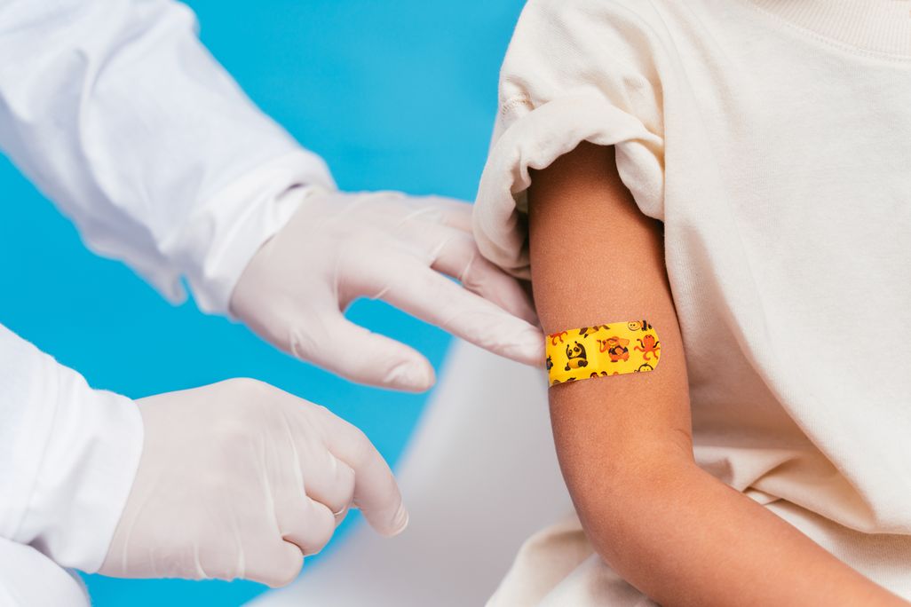 Gloved doctors hands and a child's right arm with an orange bandaid