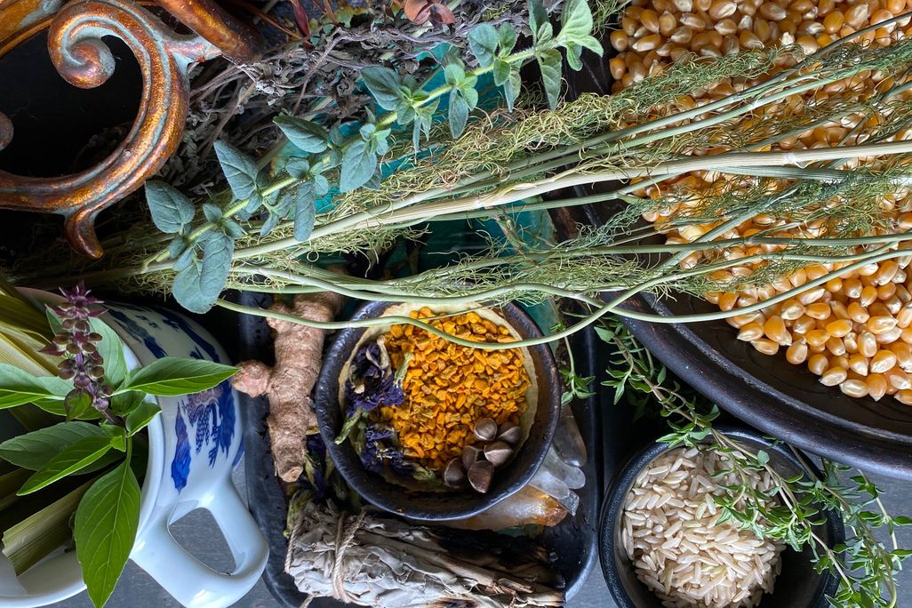 A colorful and artfully arranged assortment of herbs, spices, corn, and a white mug with blue designs clustered together on a table, viewed from above