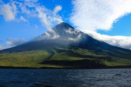 Cleveland Volcano with white clouds circling it as seen from the water on a bright, sunny day.